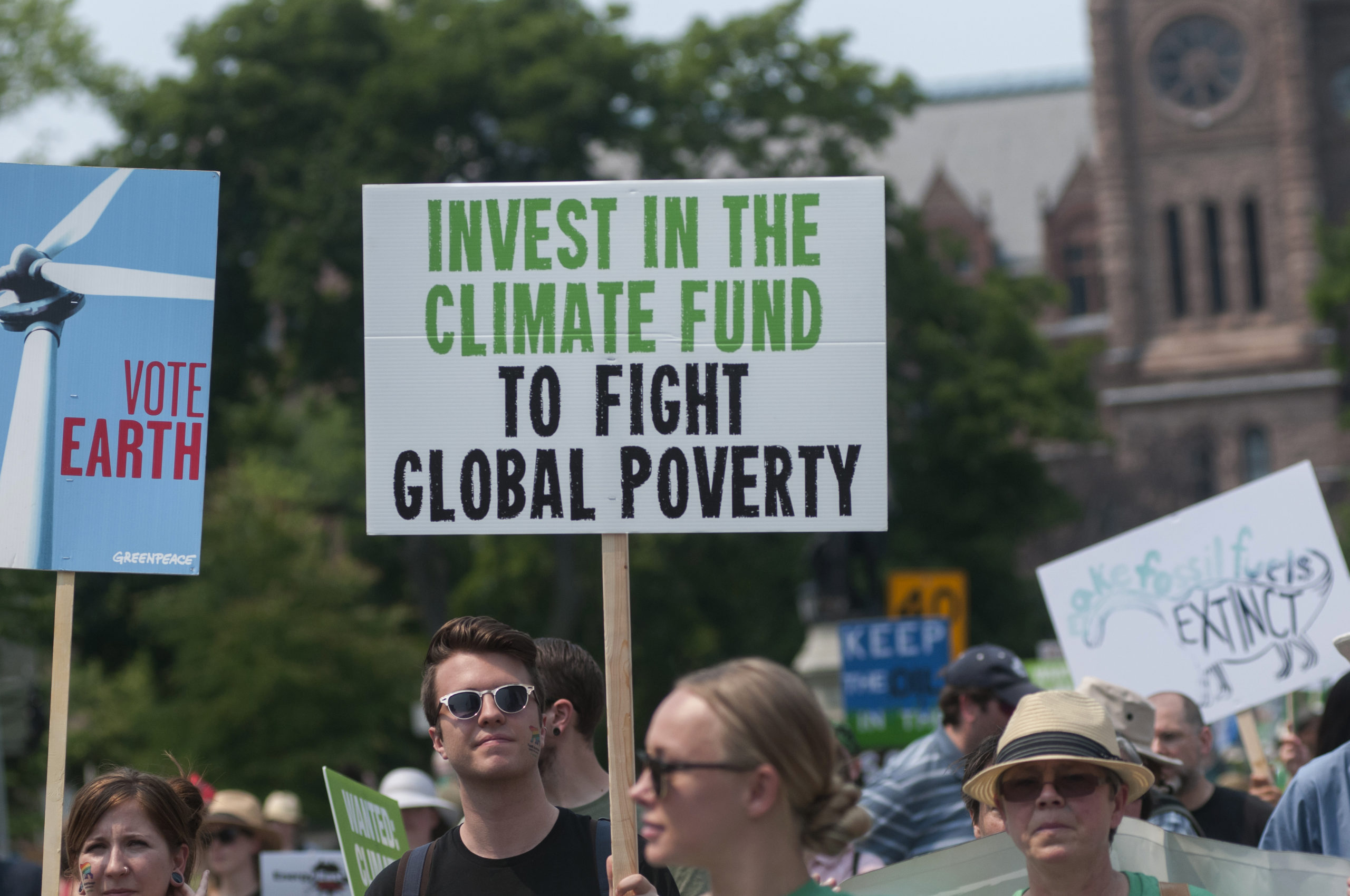 Person holds sign at a climate protest, which reads, "INVEST IN THE CLIMATE FUND TO FIGHT GLOBAL POVERTY"